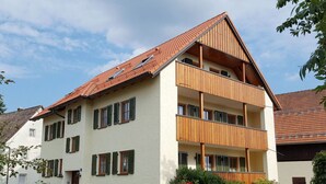 A multi-story residential building with a sloped roof, balconies, and a gated entrance.