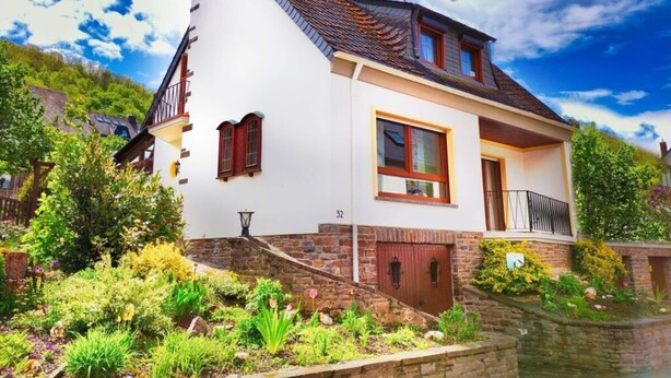A two-story house with a steeply pitched roof, a small balcony, and a stone foundation. - Vakantiehuis Mosella (Oberfell)