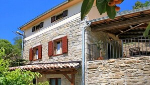 A stone building with a tiled roof, a balcony with metal railings, and a tree with green leaves and orange flowers. - Aurora Comfortable Holiday Residence (Oprtalj)
