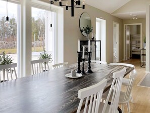 Comedor con mesa de madera oscura, sillas blancas, un espejo grande y candelabros.