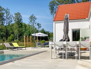 A pool area with lounge chairs and a table, a covered seating area, and a building with a red-tiled roof. - 5 Star Holiday Home in Gotlands Tofta (Gotlands Tofta)