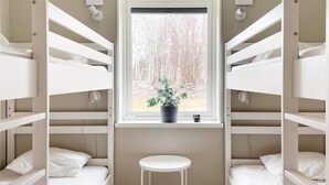 A bunk room with white bunk beds, a small white stool, a window with a view of trees, and a potted plant on the windowsill. - 5 Star Holiday Home in Gotlands Tofta (Gotlands Tofta)