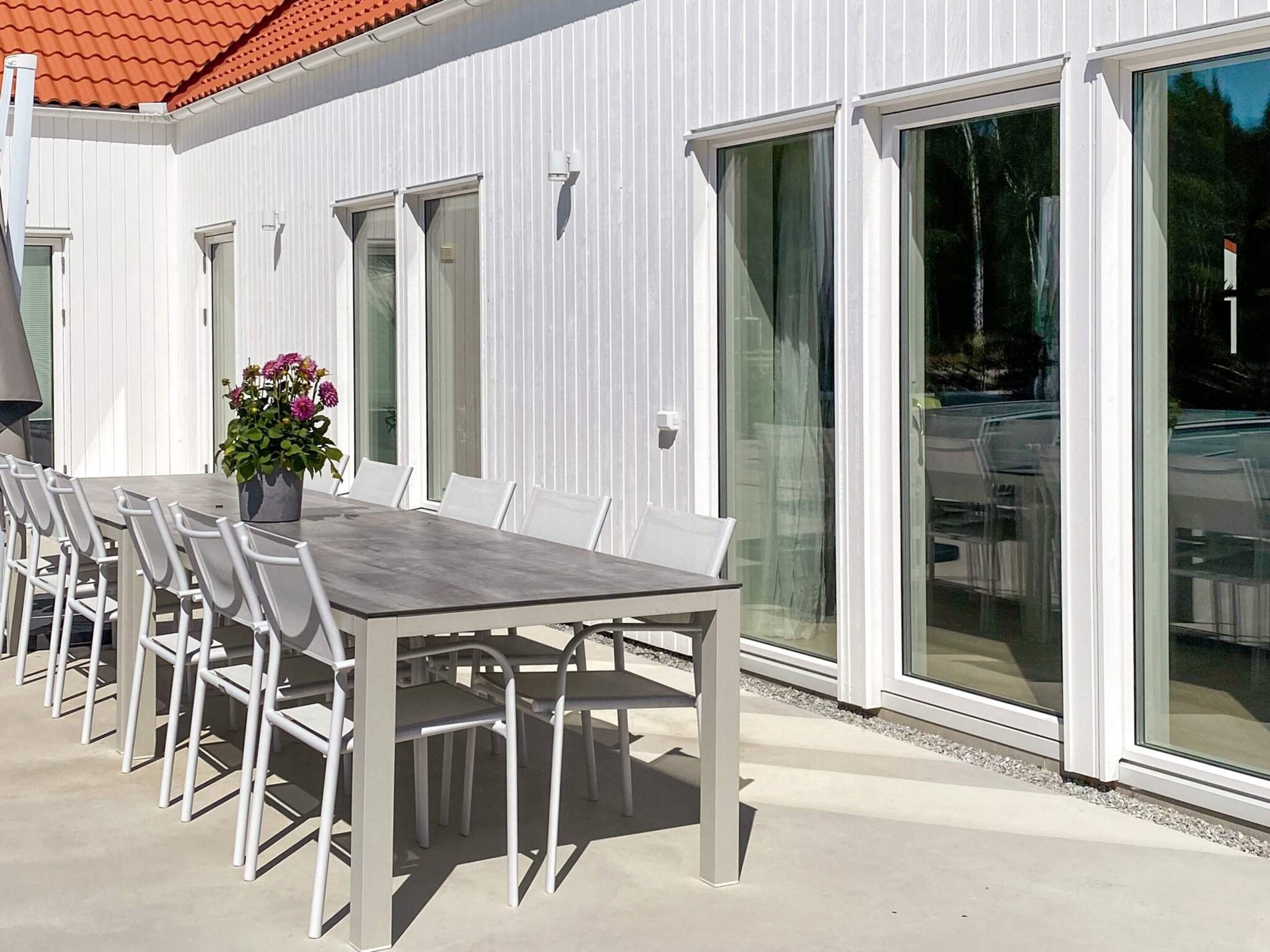 Un espace extérieur aménagé pour les repas, avec une table et des chaises, une plante en pot et une porte-fenêtre coulissante donnant sur un patio couvert.
