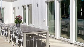 Un espace extérieur aménagé pour les repas, avec une table et des chaises, une plante en pot et une porte-fenêtre coulissante donnant sur un patio couvert.