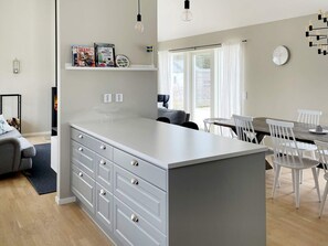 A modern kitchen with a central island, white cabinetry, and a dining area with white chairs. - 5 Star Holiday Home in Gotlands Tofta (Gotlands Tofta)