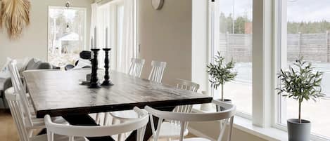 A dining area with a large wooden table, white chairs, and a view through large windows.