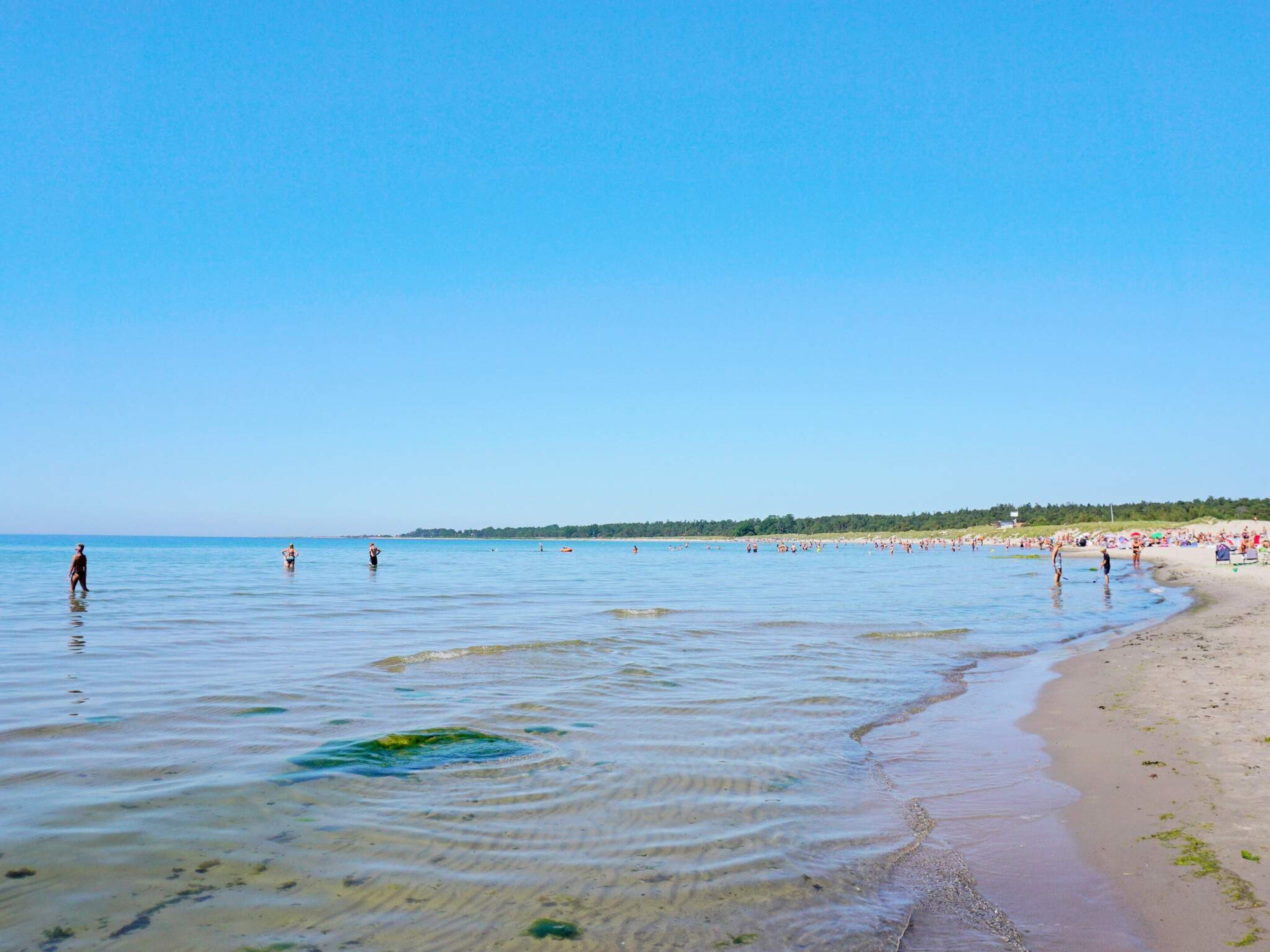 A beach with clear water, people swimming, and a sandy shore.