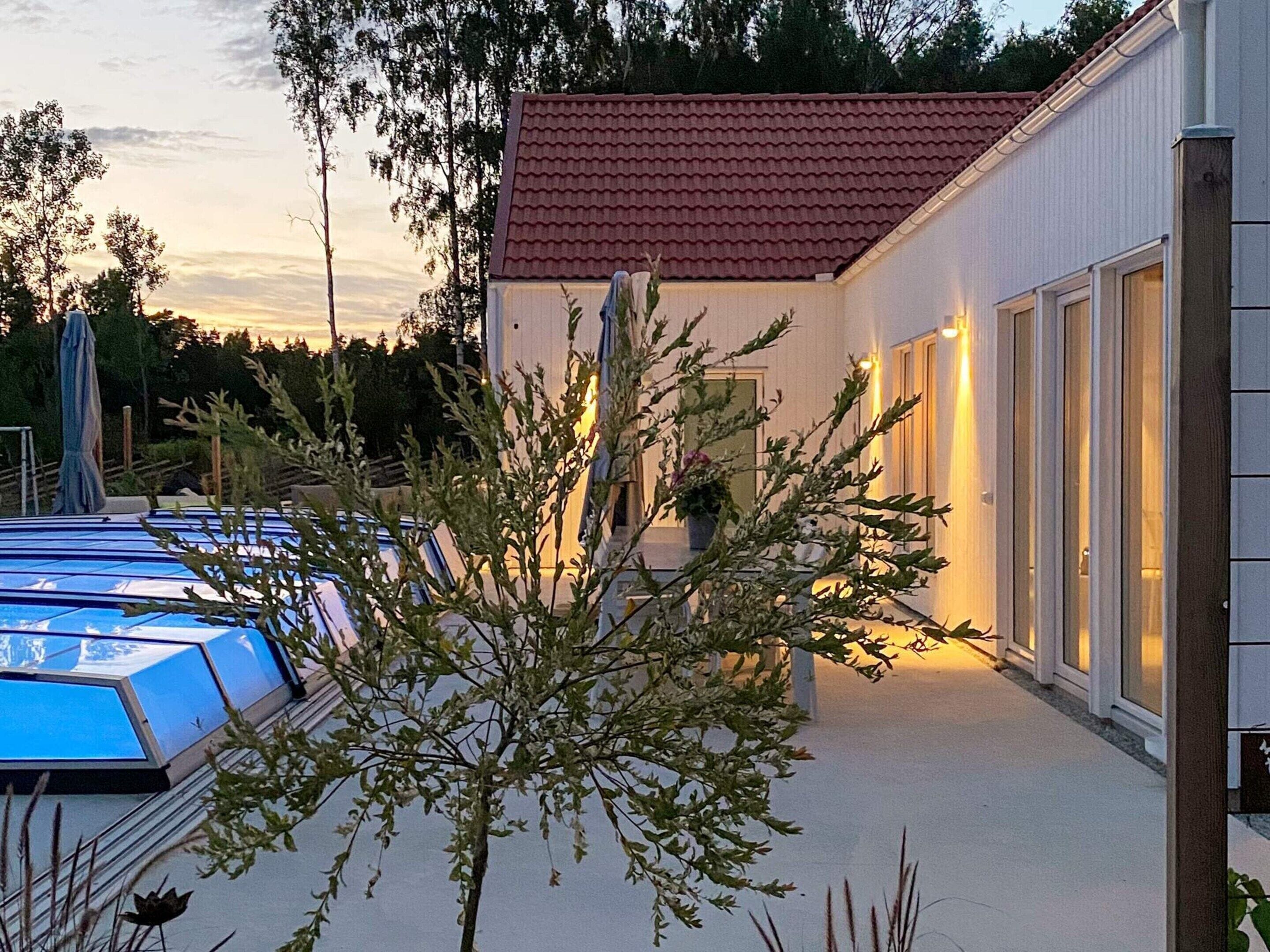 A building with a red-tiled roof, a covered outdoor area with a pool, and a tree in the foreground.