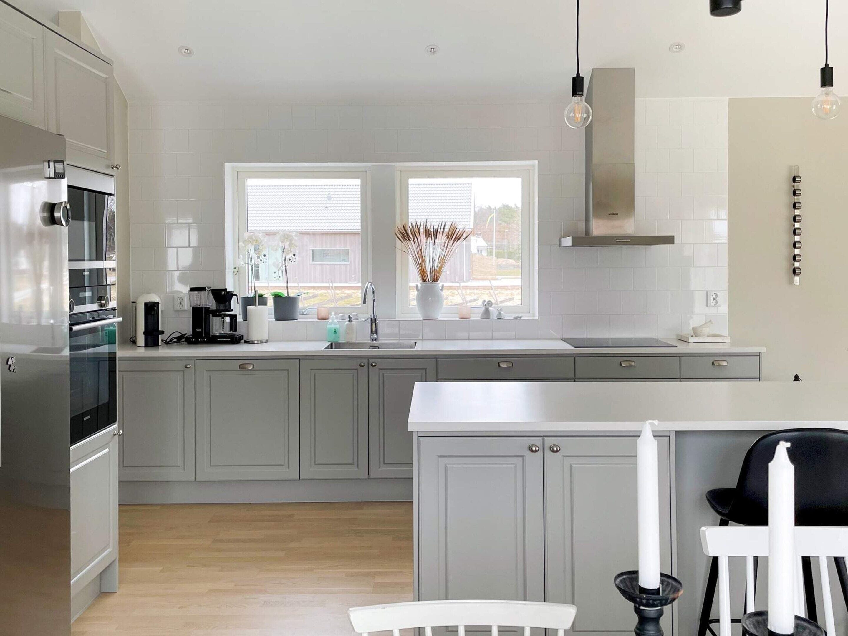 A modern kitchen with grey cabinets, a stainless steel refrigerator, a double sink, and a window with a view of the outside.