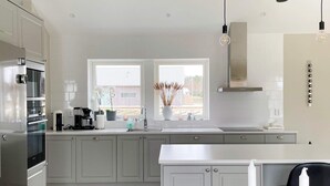A modern kitchen with grey cabinets, a stainless steel refrigerator, a double sink, and a window with a view of the outside. - 5 Star Holiday Home in Gotlands Tofta (Gotlands Tofta)