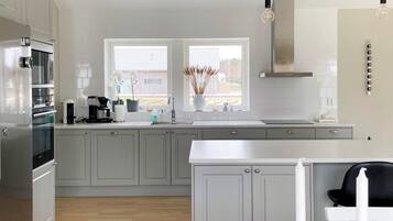 A modern kitchen with grey cabinets, a stainless steel refrigerator, a double sink, and a window with a view of the outside.