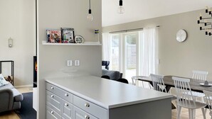 A modern kitchen with a central island, white cabinetry, and a dining area with white chairs. - 5 Star Holiday Home in Gotlands Tofta (Gotlands Tofta)