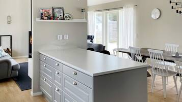 A modern kitchen with a central island, white cabinetry, and a dining area with white chairs.