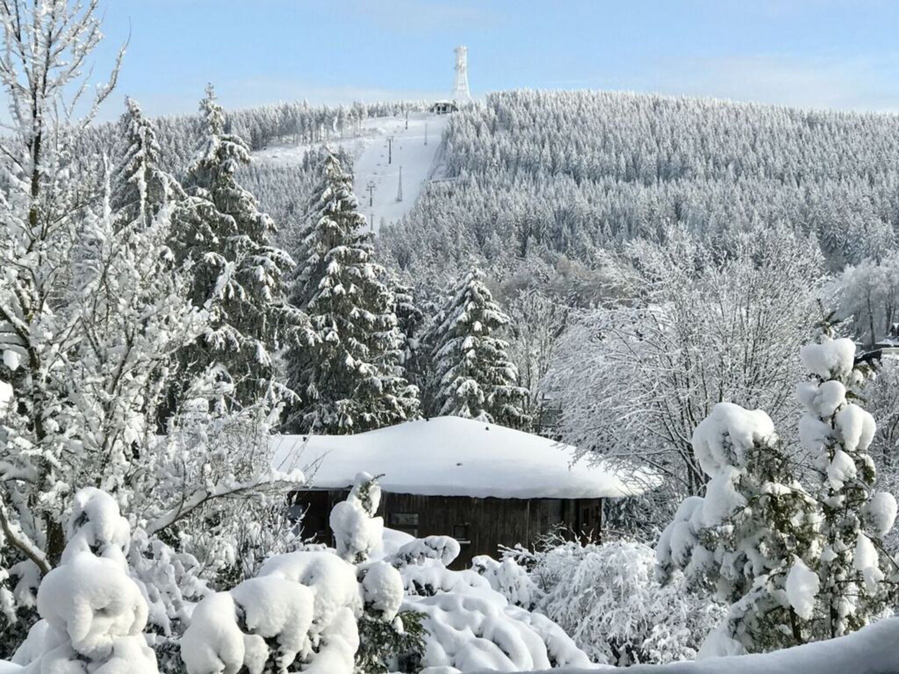 A snow-covered landscape with a cabin in the foreground and a ski slope in the background.