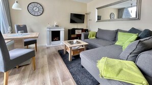 Ein modernes Wohnzimmer mit Kamin, Flachbildfernseher, einer Couch und einem Essbereich.