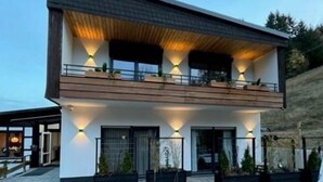 Ett modernt hus i två våningar med ett platt tak, stora fönster och en balkong.