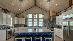A spacious kitchen with a large island, wooden ceiling, and modern appliances.