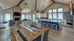 A spacious living area with a wooden ceiling, a large dining table, and a kitchen with blue and white tiles.