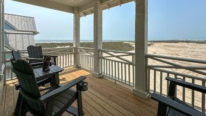 A covered deck with wooden furniture and a view of the beach.