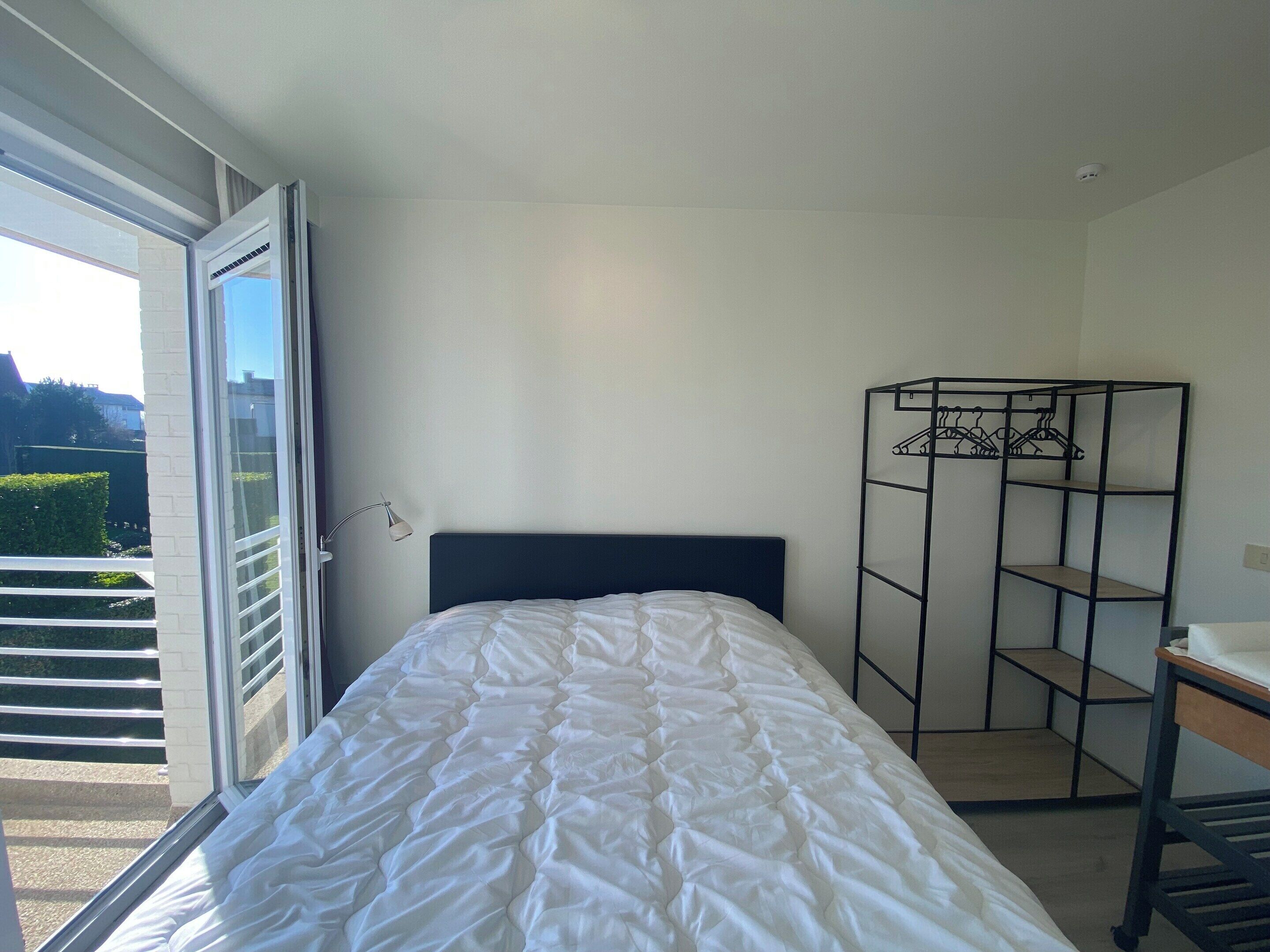 A bedroom with a bed, a metal wardrobe, and a window with a view of greenery.