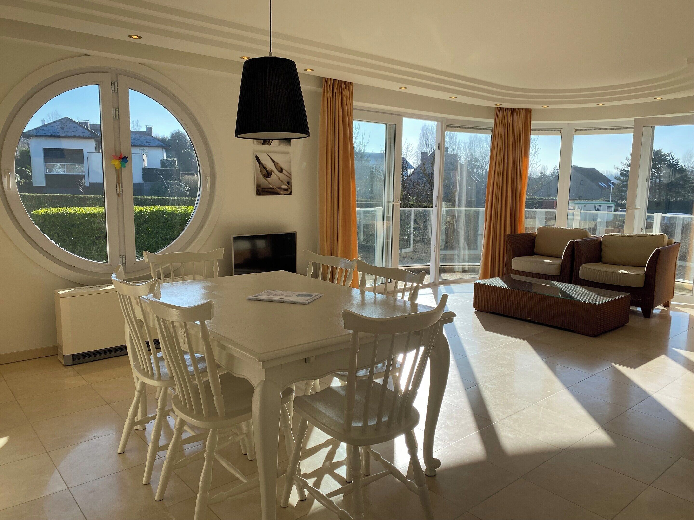 Ein geräumiges Wohnzimmer mit Essbereich, großen Fenstern und Blick auf die Nachbarschaft.