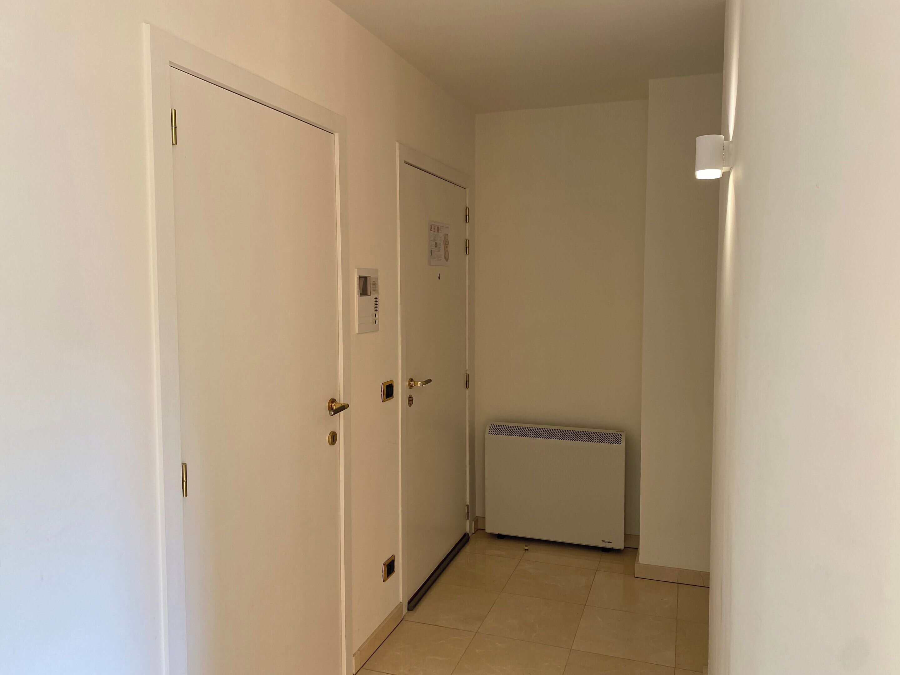 Un couloir étroit avec des portes blanches, un thermostat et un radiateur.