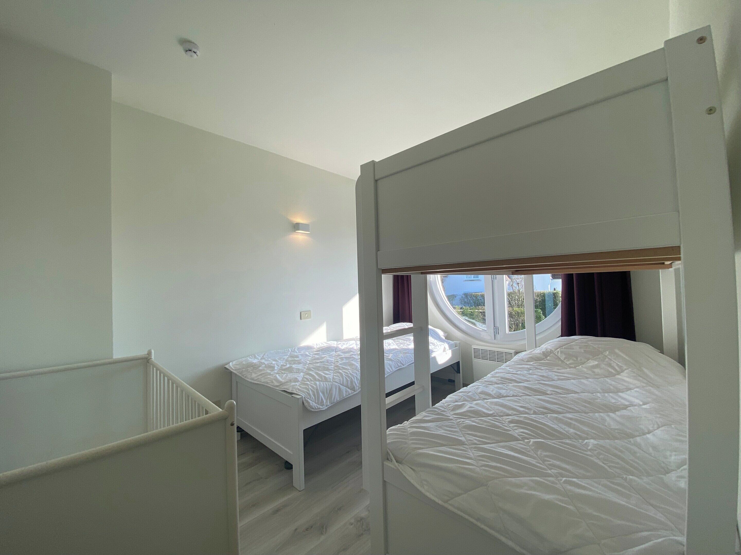 Ein Zimmer mit zwei Etagenbetten, einem Babybett und einem Fenster mit Blick nach draußen.