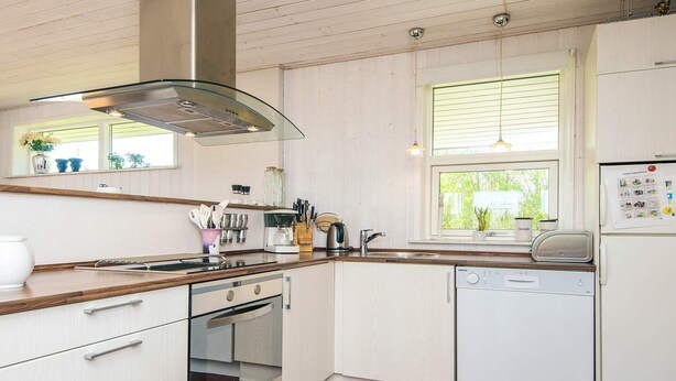 Une cuisine moderne avec des meubles blancs, un plan de travail en bois, un four encastré, un lave-vaisselle et une fenêtre donnant sur un espace verdoyant.