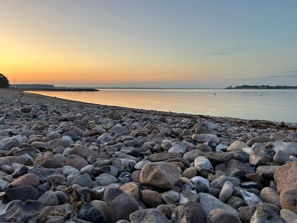 Une plage de galets, avec une eau calme et un coucher de soleil.