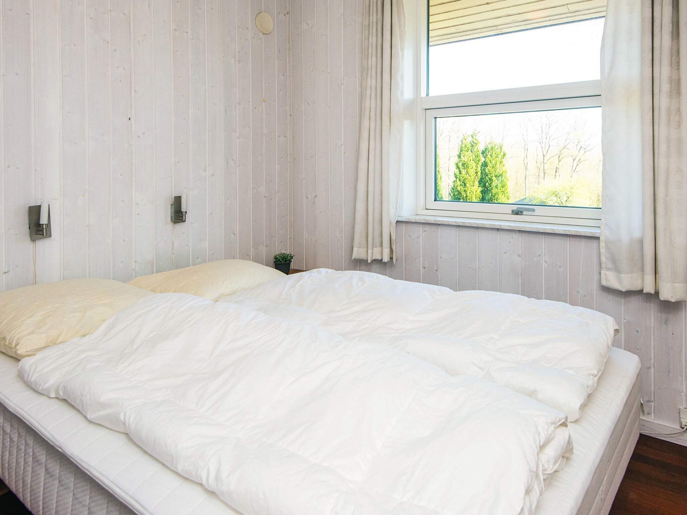 Un dormitorio con una cama grande, una ventana con cortinas y una pequeña planta en maceta sobre la mesita de noche.