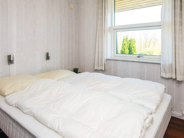 Un dormitorio con una cama grande, una ventana con cortinas y una pequeña planta en maceta sobre la mesita de noche.