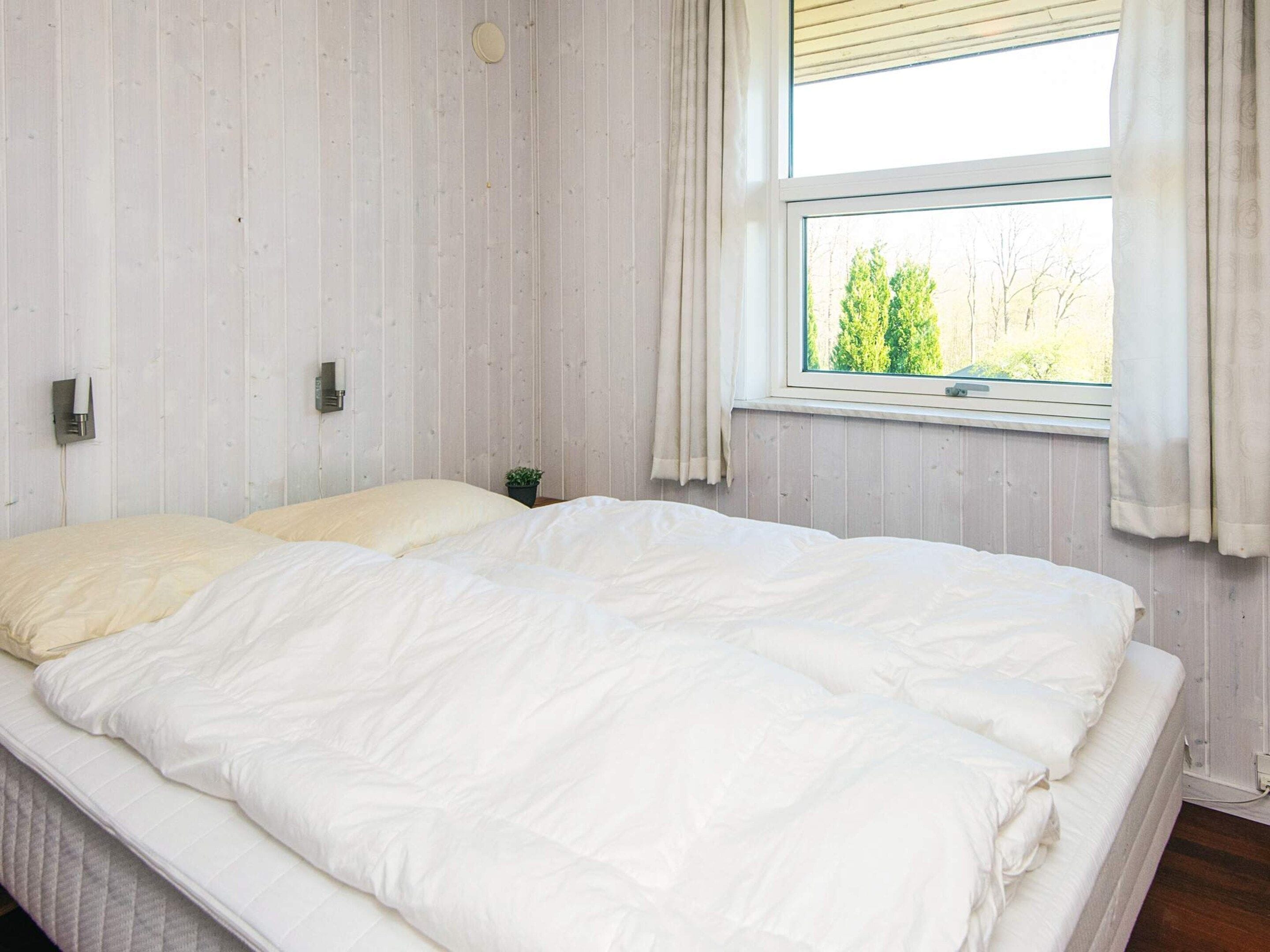 A bedroom with a large bed, a window with curtains, and a small plant on the nightstand.