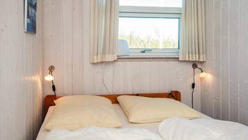 A single bed with two pillows, a window with curtains, and two wall-mounted lamps.