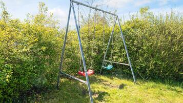 A swing set in a grassy area with dense foliage in the background.