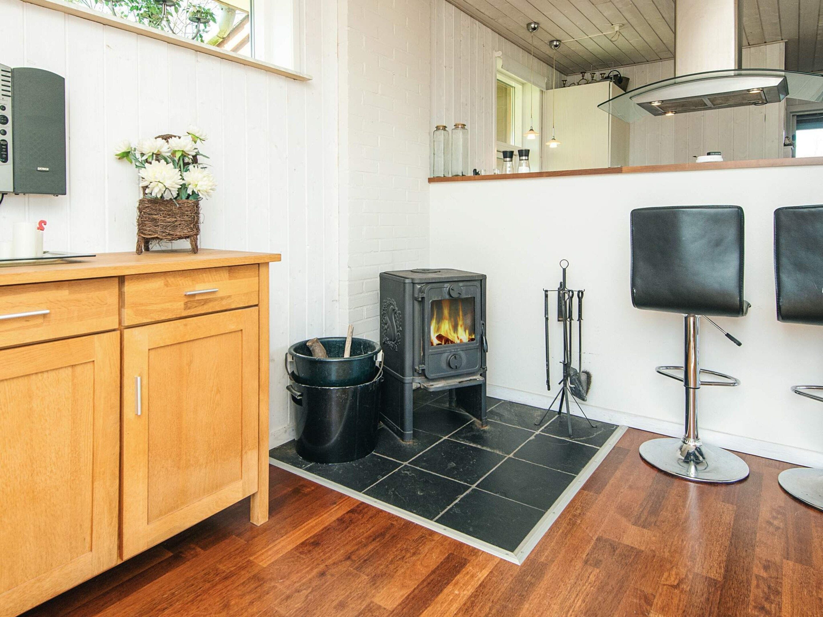Een moderne keuken met een houtgestookte kachel, houten kastjes en een vloer van zwart tegels.