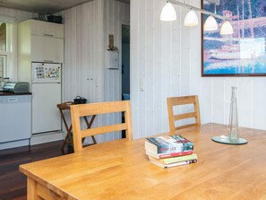 A wooden dining table with a stack of books, two chairs, a kitchen area with a refrigerator, and a painting on the wall. - 4 Person Holiday Home in Aabenraa (Aabenraa)