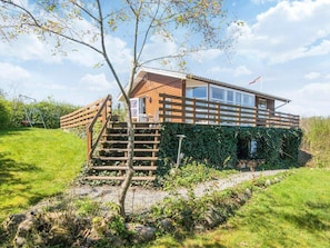 A wooden cabin with a staircase leading to a deck, surrounded by greenery and a clear sky. - 4 Person Holiday Home in Aabenraa (Aabenraa)