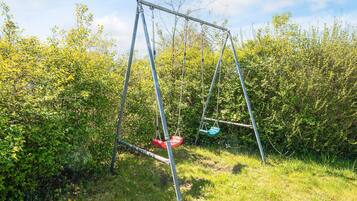 Eine Schaukelanlage in einer grünen Wiese, umgeben von dichtem Gebüsch.