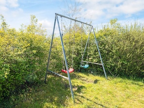 A swing set in a grassy area with dense shrubbery around it. - 4 Person Holiday Home in Aabenraa (Aabenraa)