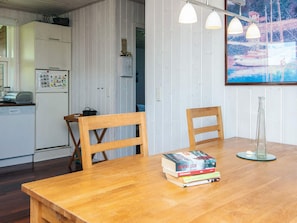 A wooden dining table with chairs, a kitchen area with white cabinets, a refrigerator, and a painting on the wall. - 4 Person Holiday Home in Aabenraa (Aabenraa)