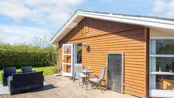 A wooden cabin with a deck, a covered outdoor seating area, and a large window.