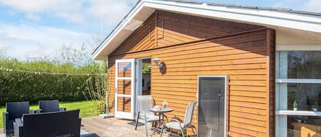 En træhytte med en terrasse, et overdækket udeområde og et stort vindue.