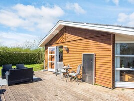 A wooden cabin with a deck, a covered outdoor seating area, and a large window.