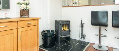 A modern kitchen with a wood-burning stove, wooden cabinets, and a black tiled floor.