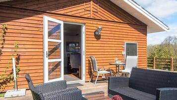 A wooden cabin with a deck, outdoor seating, and a sliding glass door leading to an interior space.