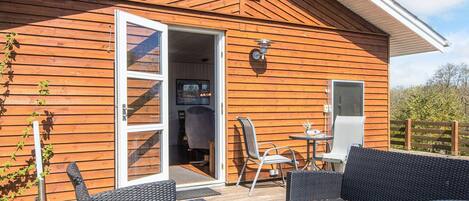 A wooden cabin with a deck, outdoor seating, and a sliding glass door leading to an interior space.