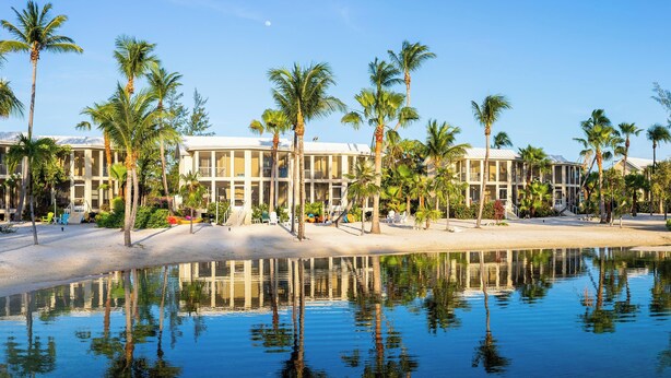 Een resort met meerdere gebouwen, palmbomen en een reflecterend waterlichaam.