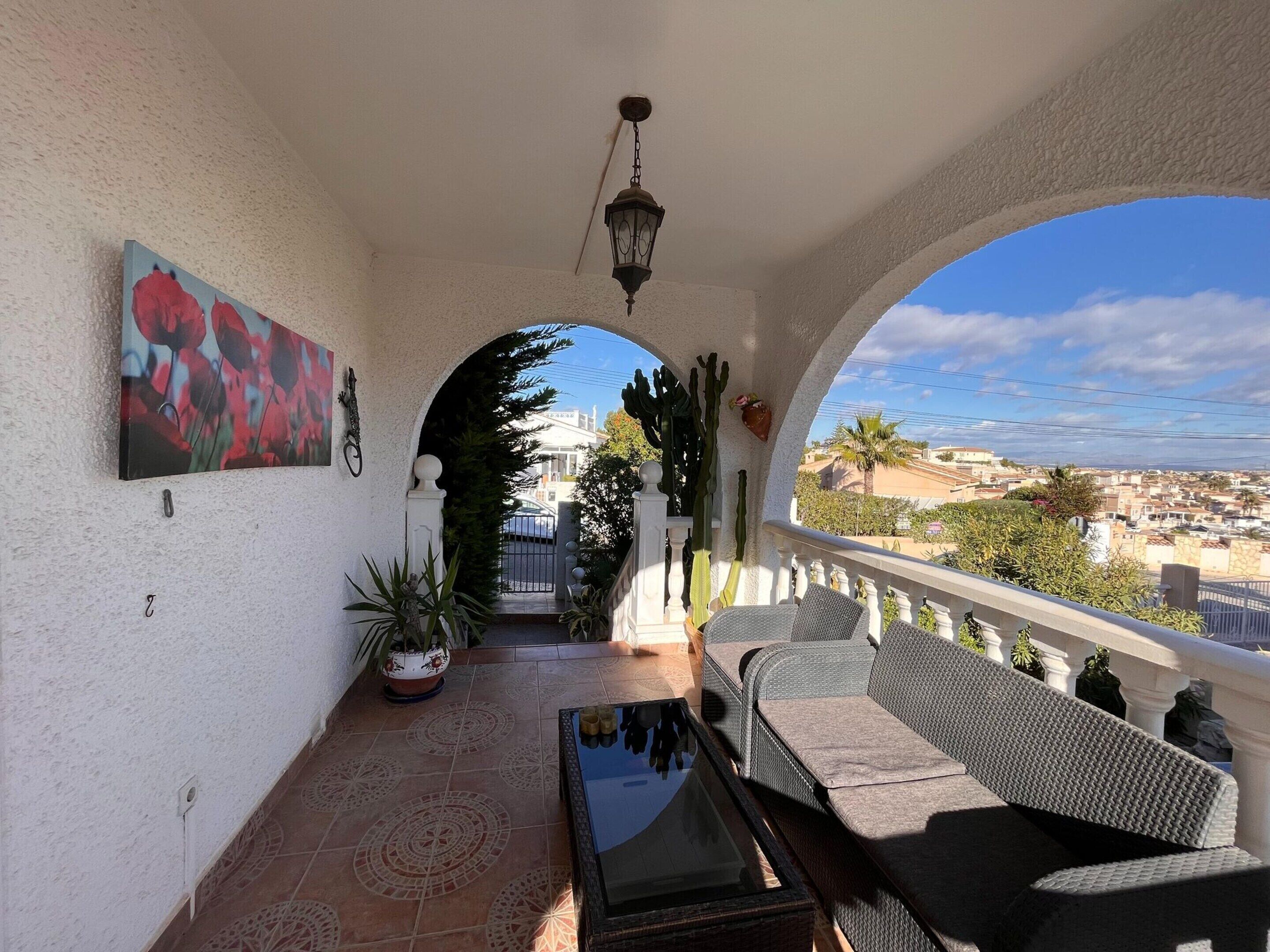 A covered balcony with a view of the city, a painting on the wall, and a cactus decoration.