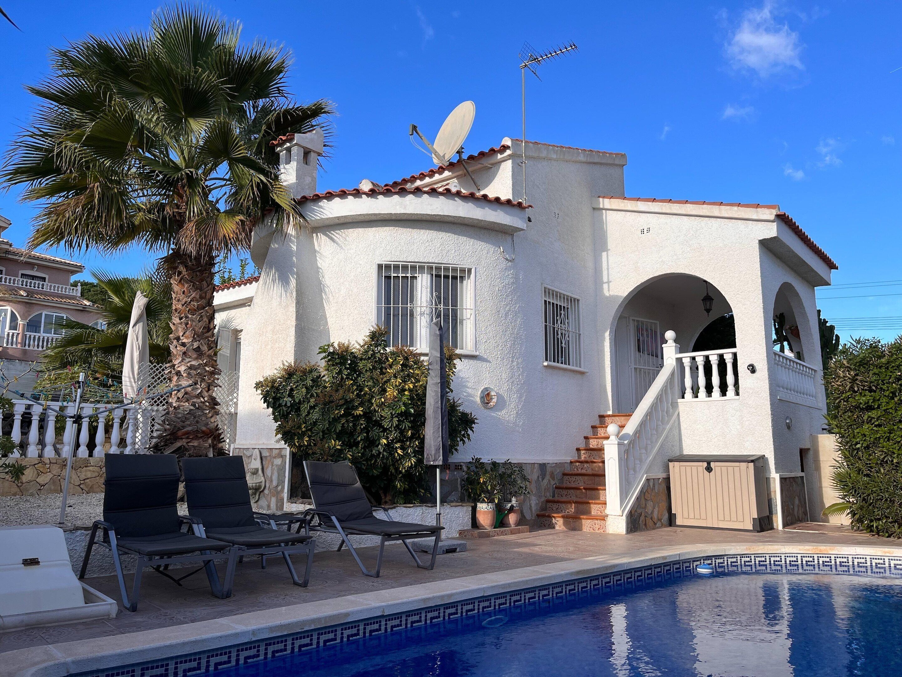 Een witte villa met een zwembad, een schotelantenne en een trap naar een balkon.