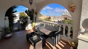 A covered outdoor seating area with a glass-top table and wicker chairs, overlooking a cityscape. - Costa Blanca Poolside Bliss (Rojales)